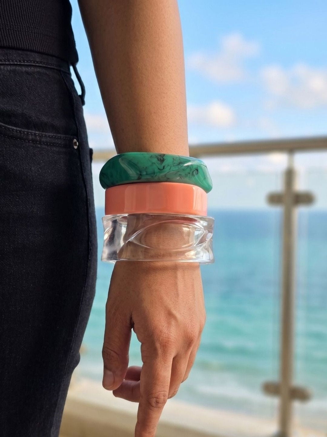 Side view of three stacked resin bangles worn on a wrist with ocean and sky in the background