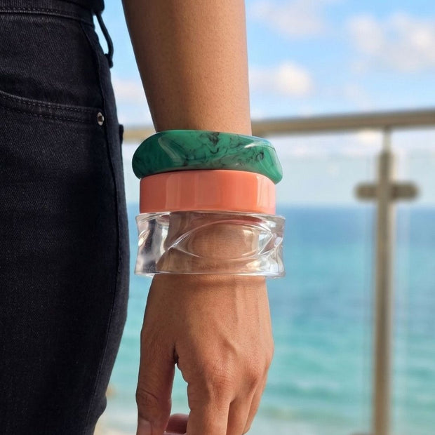 Side view of three stacked resin bangles worn on a wrist with ocean and sky in the background