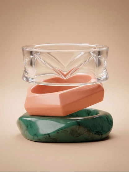 Clear acrylic, coral-pink and marbled green resin bangles stacked vertically on a beige studio background