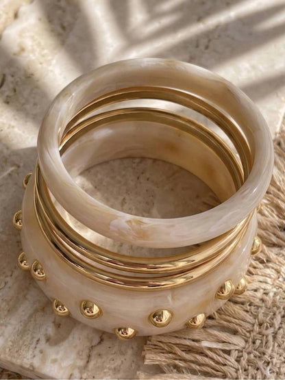 Five ivory marble resin and gold-plated bangles stacked together on a stone surface in warm light