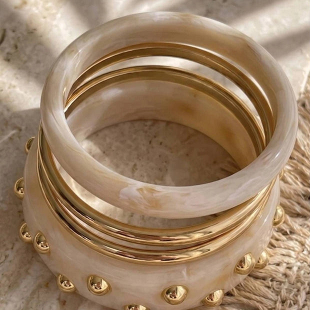Five ivory marble resin and gold-plated bangles stacked together on a stone surface in warm light