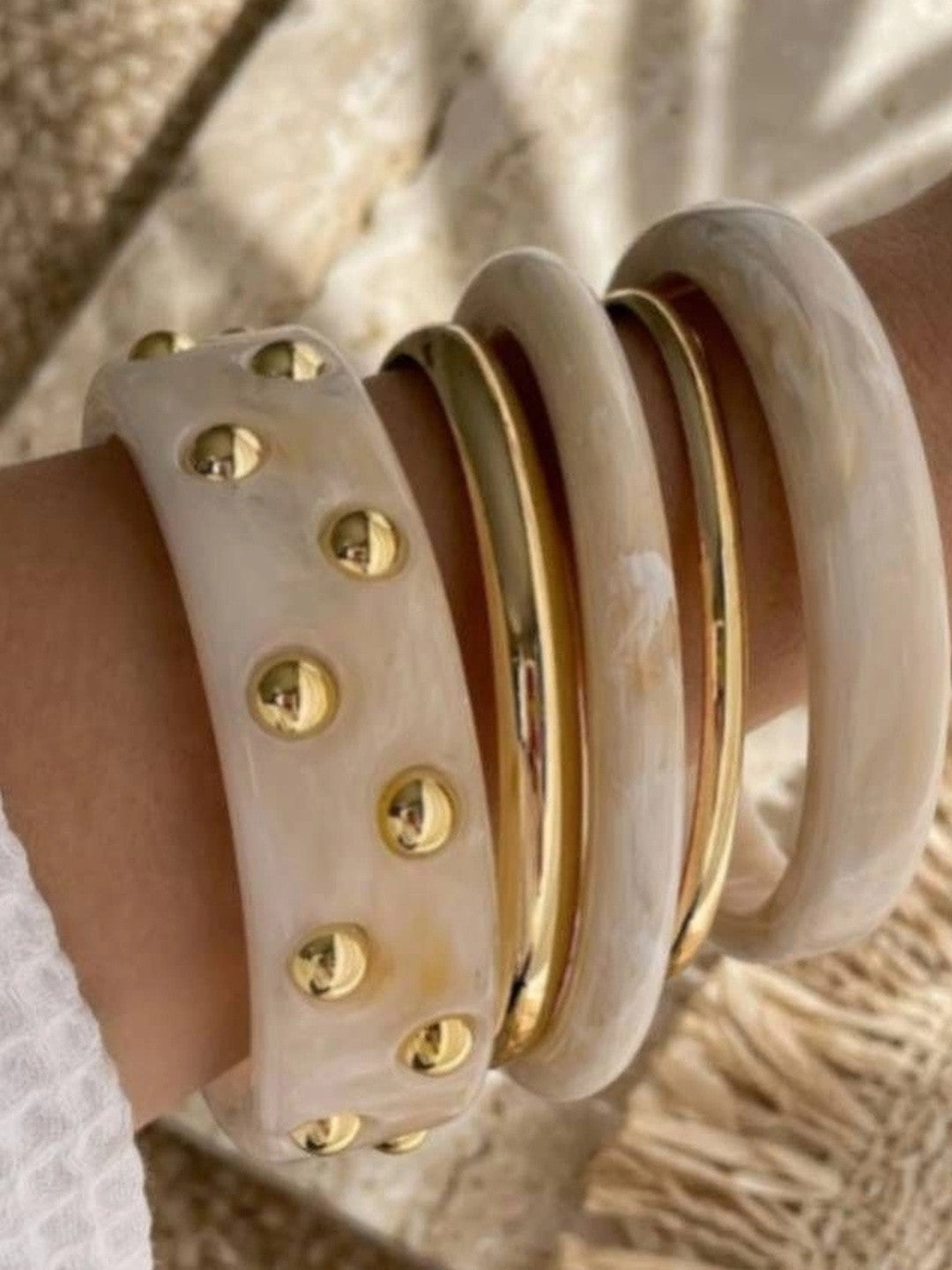 Close-up of the five-bangle stack worn on a wrist showing wide studded cuff and slim gold metal bangles