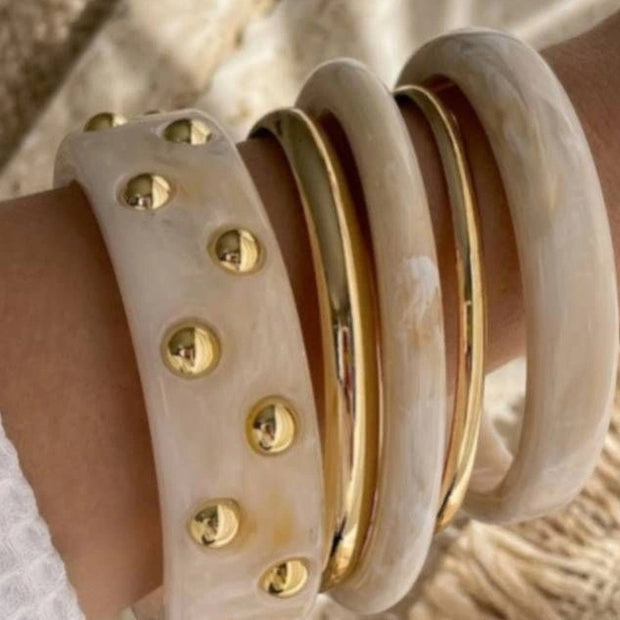 Close-up of the five-bangle stack worn on a wrist showing wide studded cuff and slim gold metal bangles