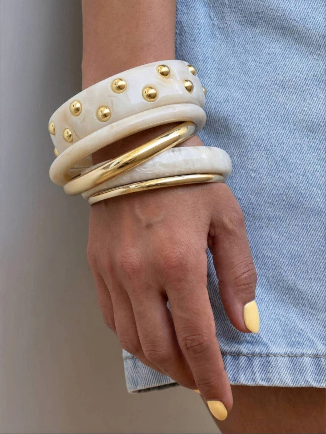 Full five-bangle stack on a wrist against a denim background showing gold studs and metal bangle details