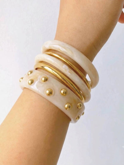 Side view of the complete bangle stack on a wrist highlighting the layered ivory resin and gold-plated metal bangles