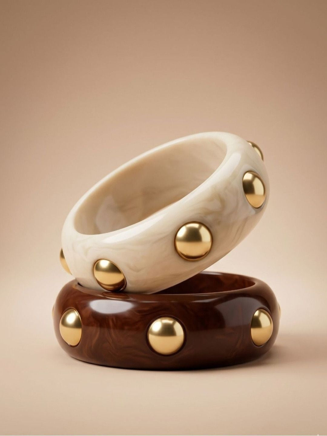 Ivory marble and chocolate brown resin bangles with gold dome studs stacked on a beige surface