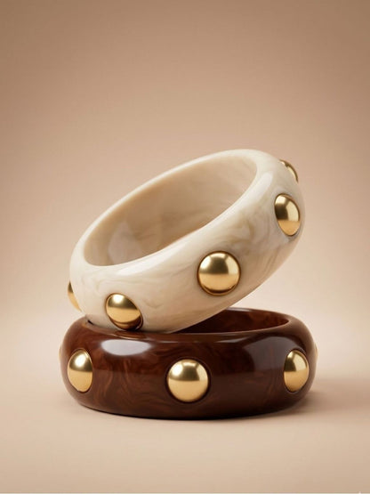 Ivory marble and chocolate brown resin bangles with gold dome studs stacked on a beige surface