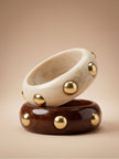 Ivory marble and chocolate brown resin bangles with gold dome studs stacked on a beige surface