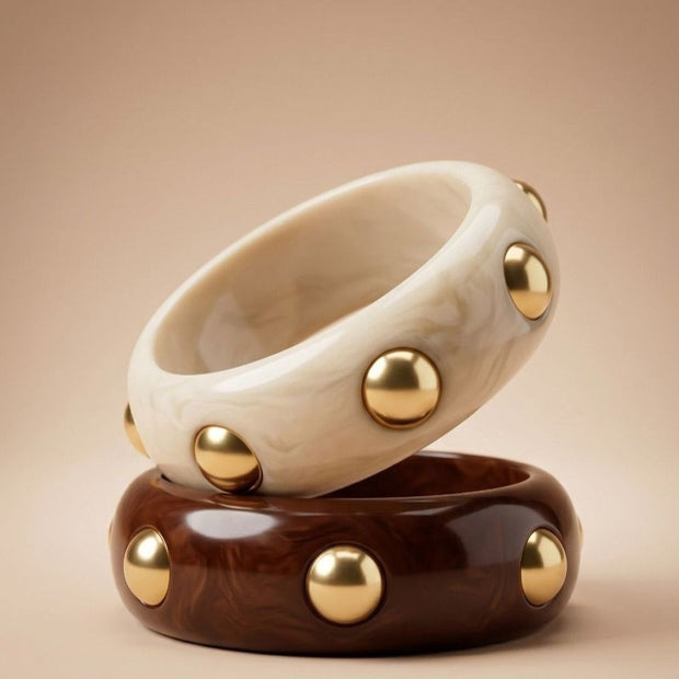 Ivory marble and chocolate brown resin bangles with gold dome studs stacked on a beige surface