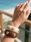 Both gold-studded resin bangles worn stacked on a wrist against a bright ocean backdrop