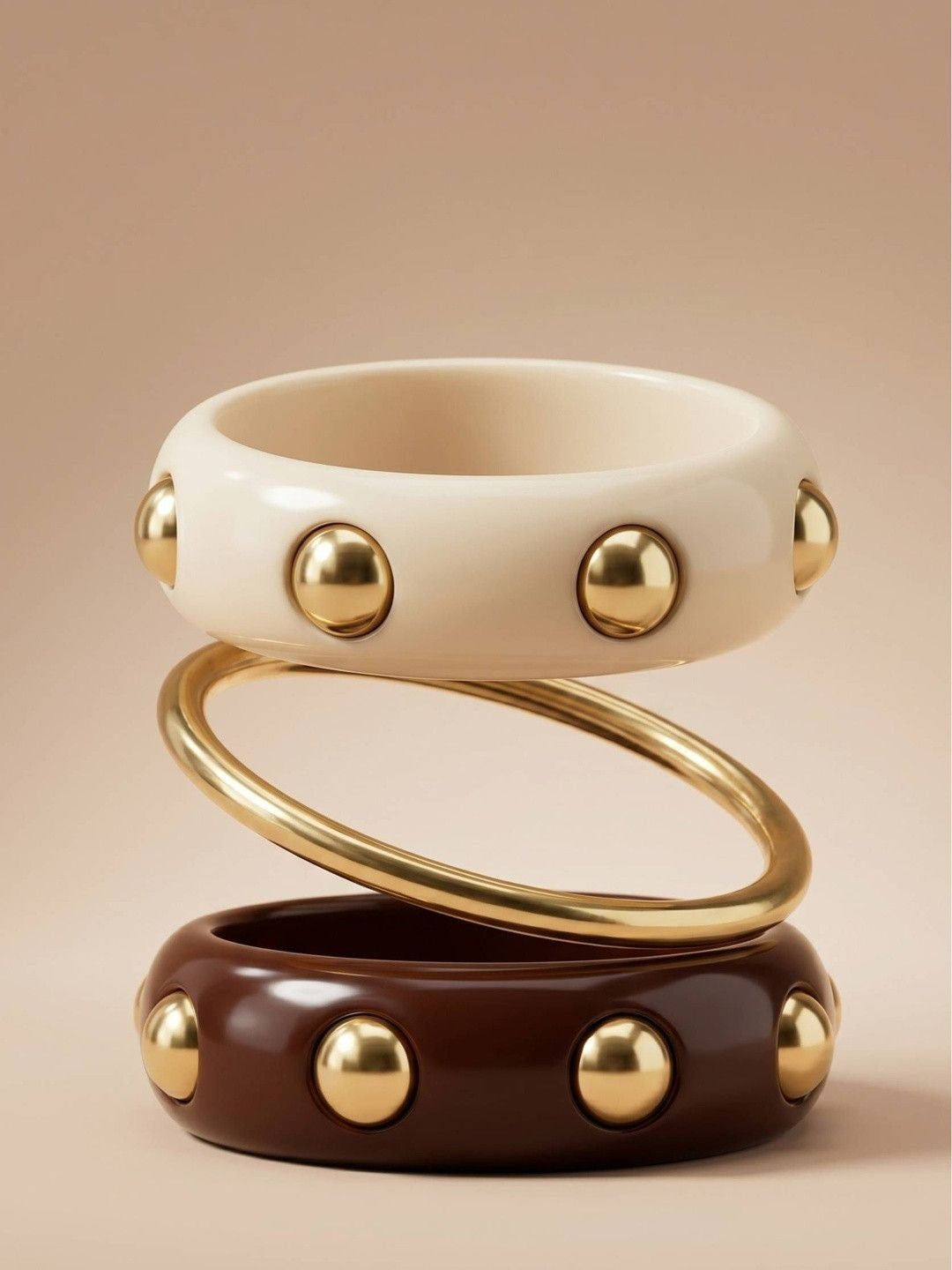 Cream resin bangle with gold studs stacked above a gold-tone slim bangle and a burgundy stud bangle on a neutral background