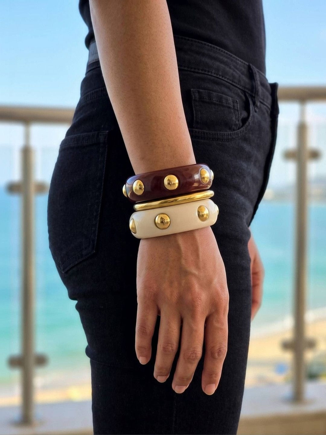 Model wearing the three-bangle stack on her wrist against a black outfit with an ocean view in the background