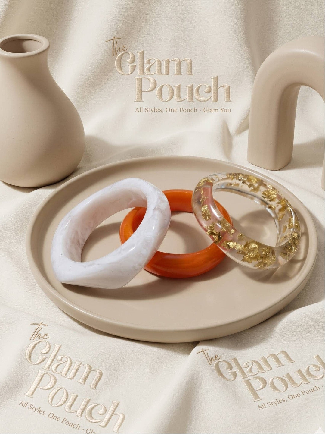 White marble, orange, and clear gold-foil resin bangles arranged on a beige tray with branded pouches