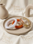 White marble, orange, and clear gold-foil resin bangles arranged on a beige tray with branded pouches