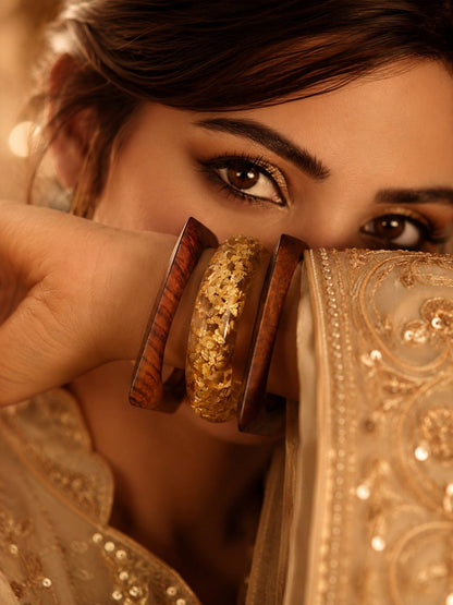 Close-up of woman in embroidered ivory lehenga holding gold foil resin and wood bangles near her face