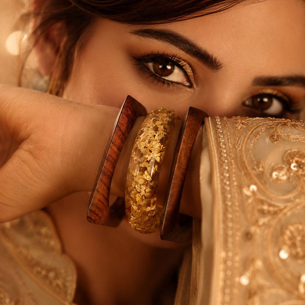 Close-up of woman in embroidered ivory lehenga holding gold foil resin and wood bangles near her face