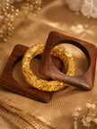Two square wooden kadas and one round gold foil resin bangle laid on a wooden tray with dried flowers