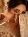Woman in cream embroidered outfit holding gold foil resin and wood bangles stacked on her wrist near her face