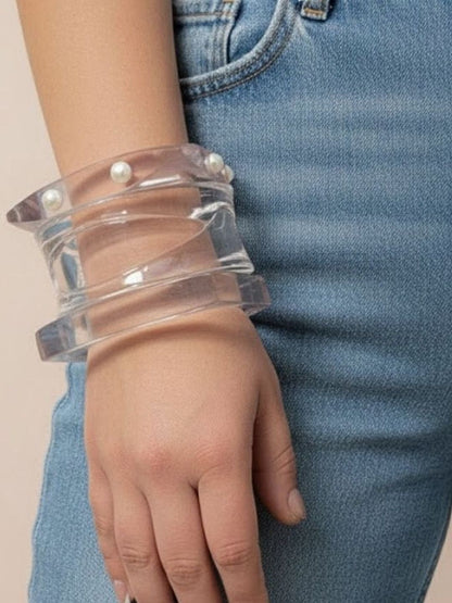 Three clear acrylic pearl stud bangles stacked on a woman's wrist against blue denim jeans