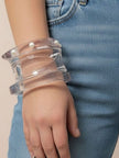 Three clear acrylic pearl stud bangles stacked on a woman's wrist against blue denim jeans