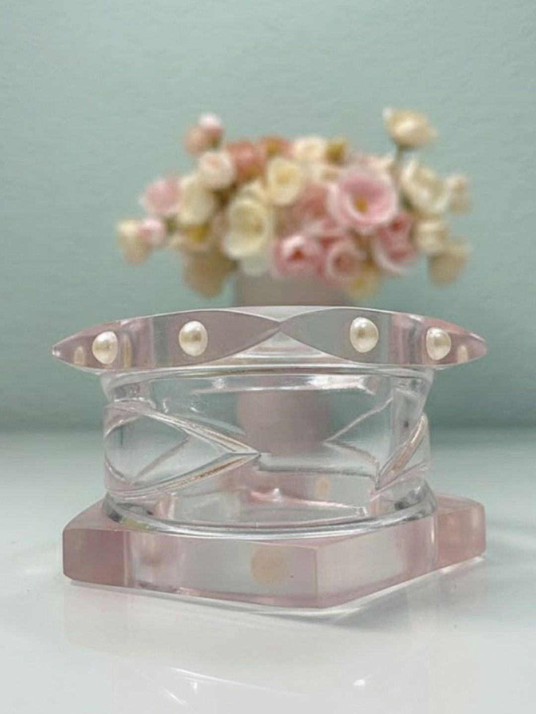 Clear and blush acrylic bangles stacked flat on a white surface with soft pink flowers in background