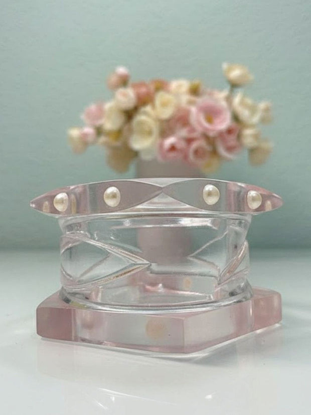 Clear and blush acrylic bangles stacked flat on a white surface with soft pink flowers in background