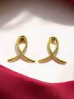 Pair of gold-plated ribbon loop stud earrings on a white surface with red fabric in the background