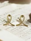 Gold-plated ribbon loop stud earrings resting on an open book with handwritten pages