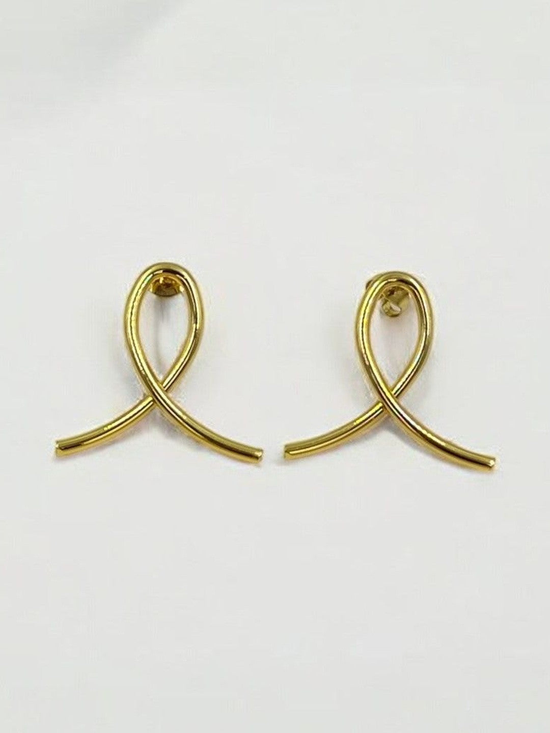 Close-up of gold-plated ribbon loop stud earrings on a white surface showing push-back posts