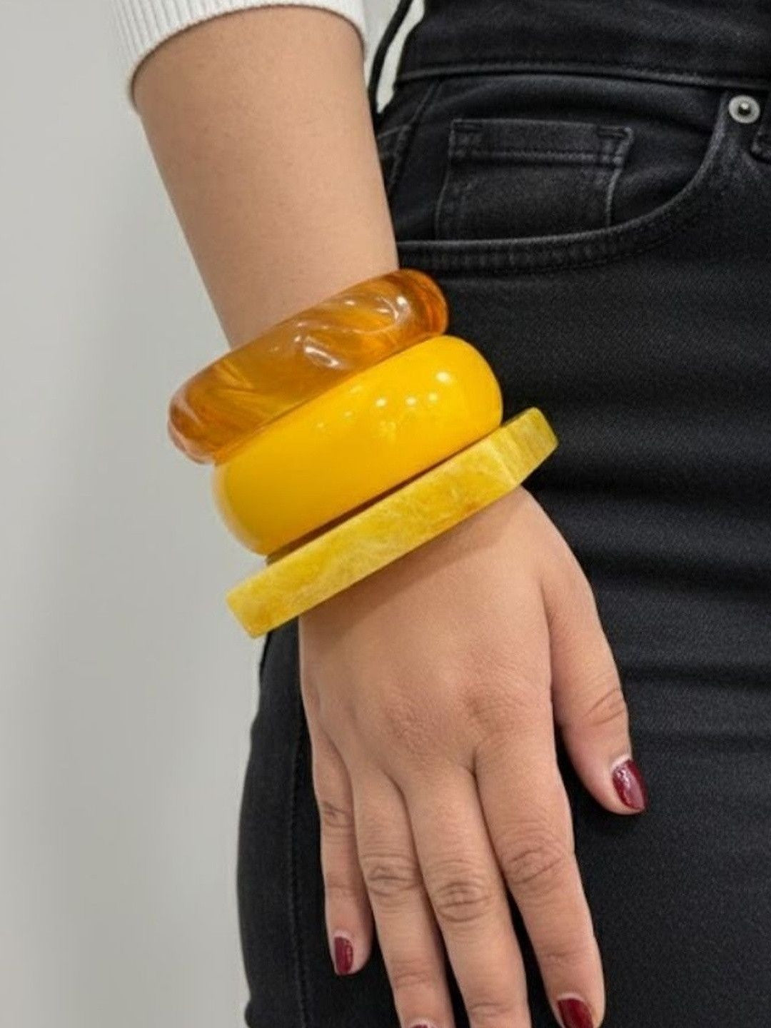 Three stacked amber and yellow resin bangles worn on a woman's wrist against a black outfit