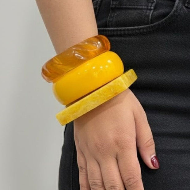 Three stacked amber and yellow resin bangles worn on a woman's wrist against a black outfit