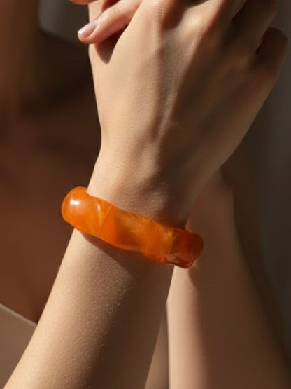 Orange marbled resin bangle worn on a woman's wrist against a warm brown background