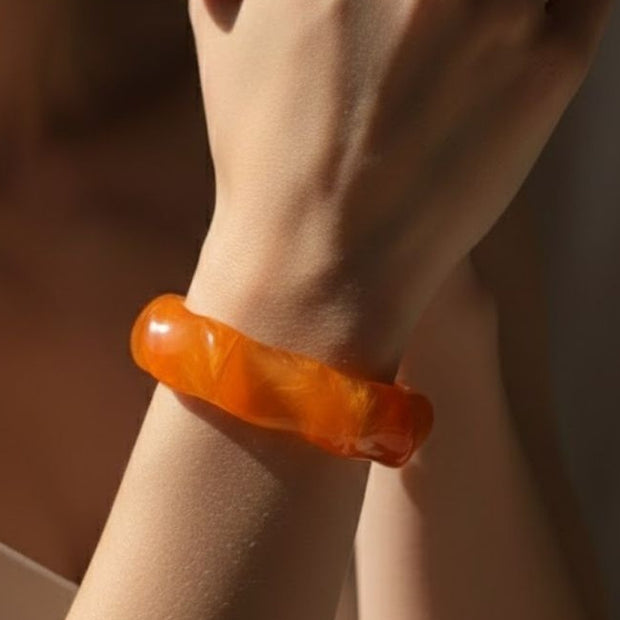 Orange marbled resin bangle worn on a woman's wrist against a warm brown background
