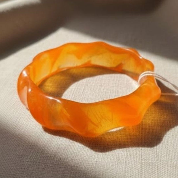 Single orange translucent resin wavy bangle resting on white linen fabric in natural light