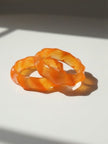 Two orange resin wavy bangles stacked together on a white surface with soft shadows