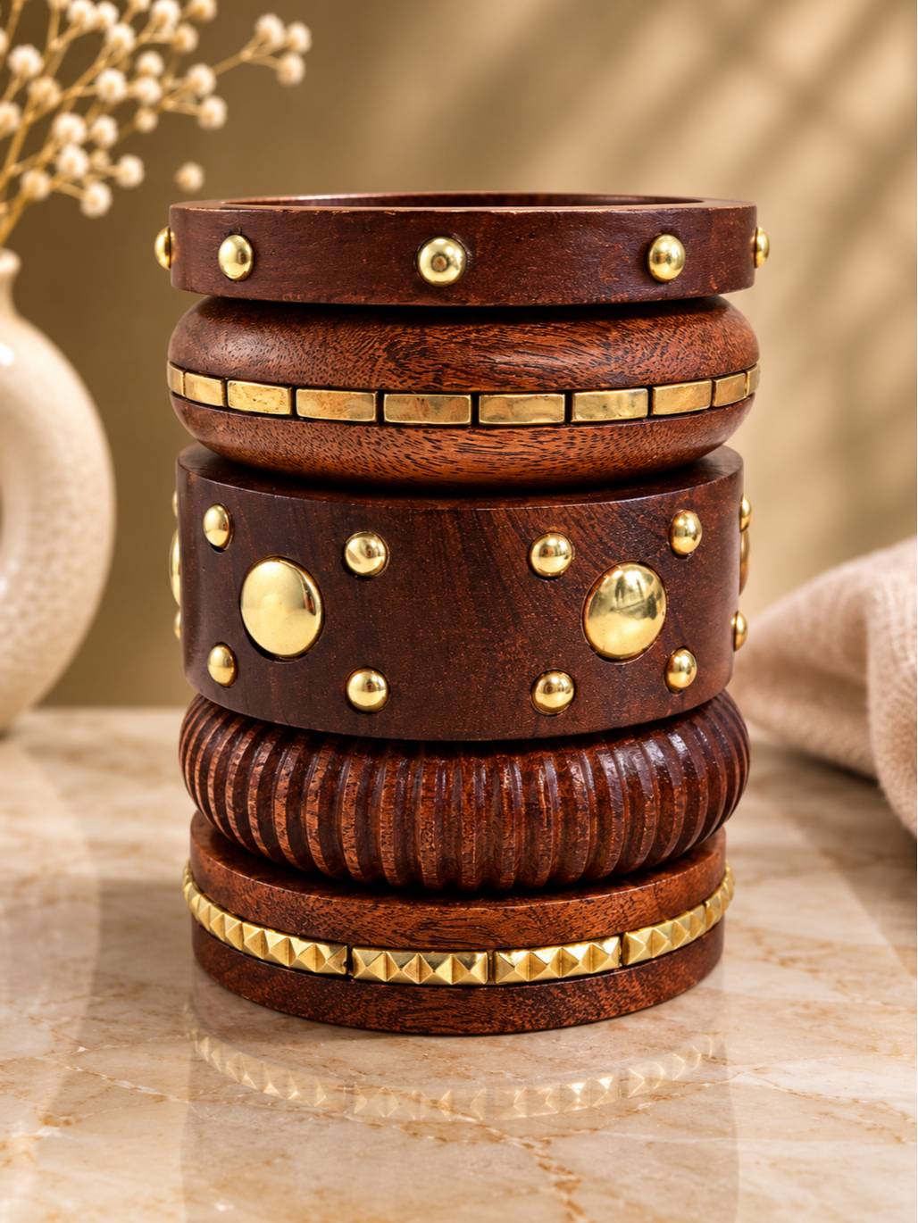 Five dark wooden bangles stacked vertically showing brass dome studs, tile inlays, ribbed carving and pyramid studs on a marble surface