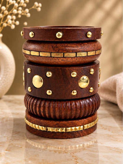 Five dark wooden bangles stacked vertically showing brass dome studs, tile inlays, ribbed carving and pyramid studs on a marble surface