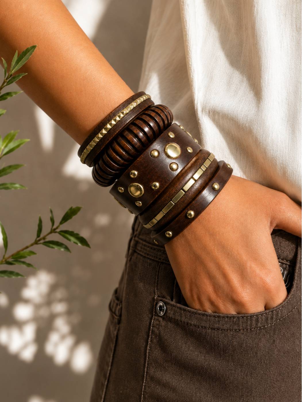 Woman wearing stacked dark wood and brass bangles on her wrist with hand in pocket of brown jeans and white top