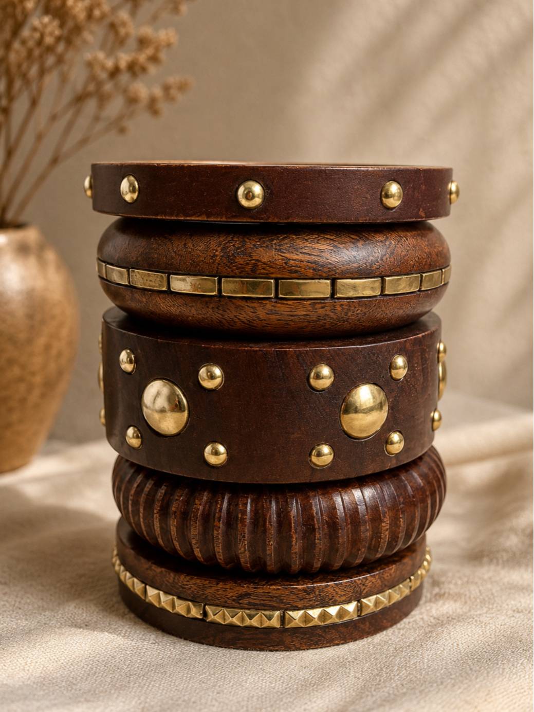 Dark wooden bangles stacked in a tower on linen cloth with an earthen vase in the background showing brass embellishment detail