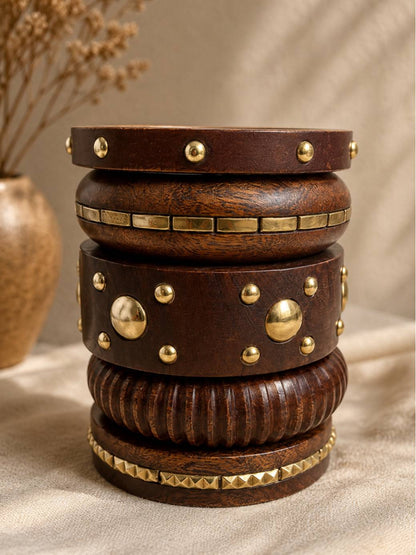 Dark wooden bangles stacked in a tower on linen cloth with an earthen vase in the background showing brass embellishment detail