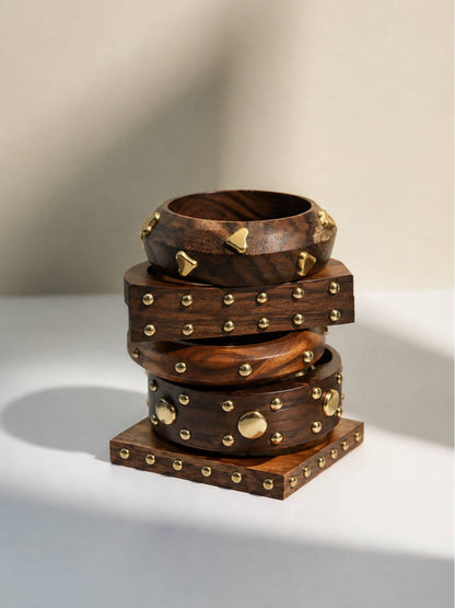Stack of four brass-studded dark wooden bangles with varied stud shapes on a white surface