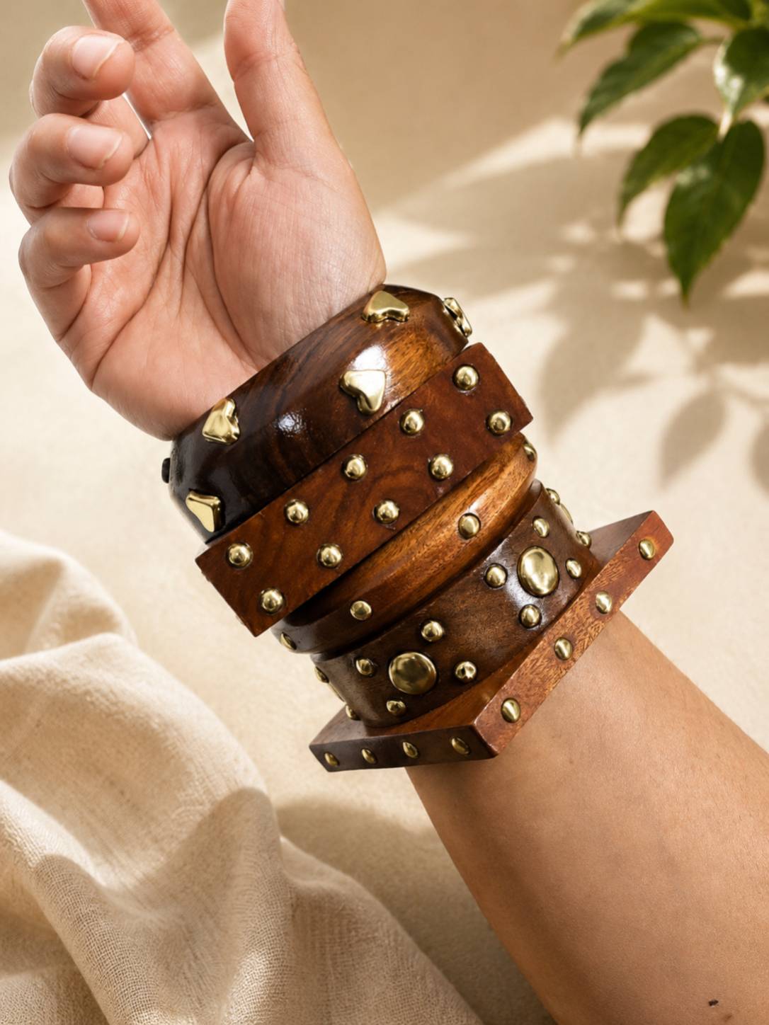 All four wooden bangles stacked together on a woman's raised wrist against a beige linen background
