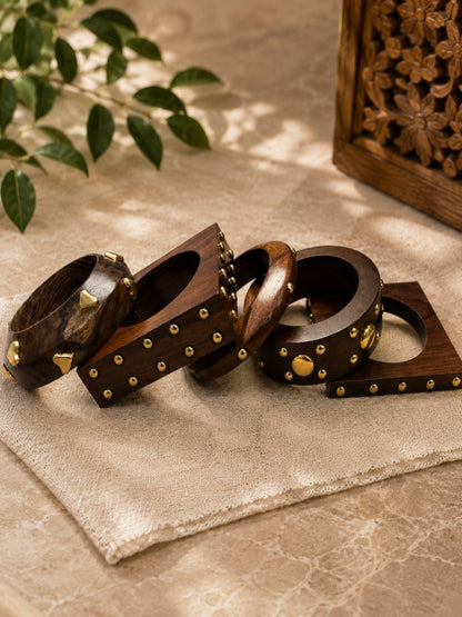 Four individual wooden bangles laid flat on linen cloth showing round, square-edged and mixed-stud designs