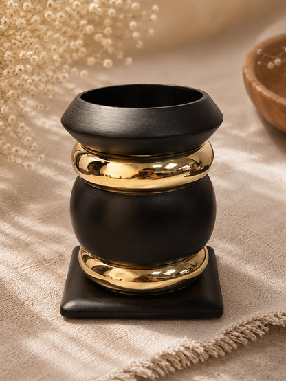 Assembled matte black and gold-tone bangle stack styled as a vase with dried flowers on a linen cloth