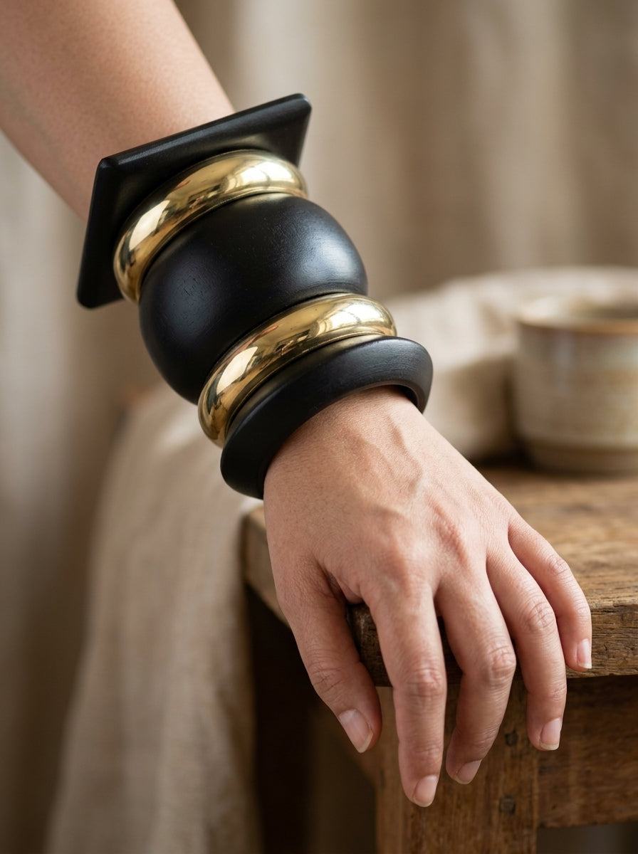 Close-up of matte black and gold-tone bangle stack worn on a woman's wrist resting on a wooden surface