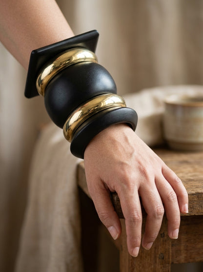 Close-up of matte black and gold-tone bangle stack worn on a woman's wrist resting on a wooden surface