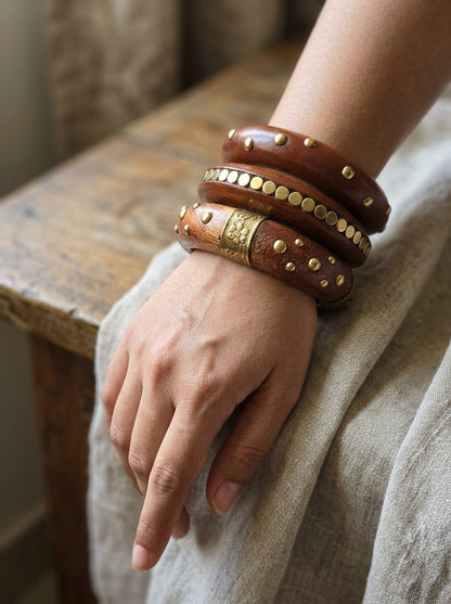 All three wooden bangles with brass detailing stacked and worn on a woman's wrist over a linen sleeve