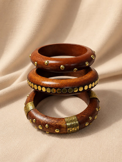 Three wooden bangles with dome studs, flat coin row and engraved brass panel stacked on a cream fabric background