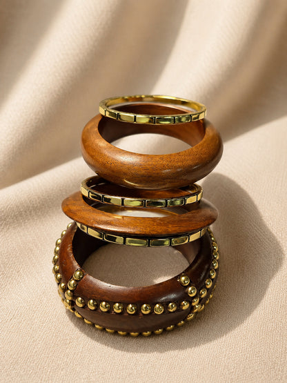 Stack of three wooden bangles showing gold tile edging and gold bead detailing against a draped beige fabric background
