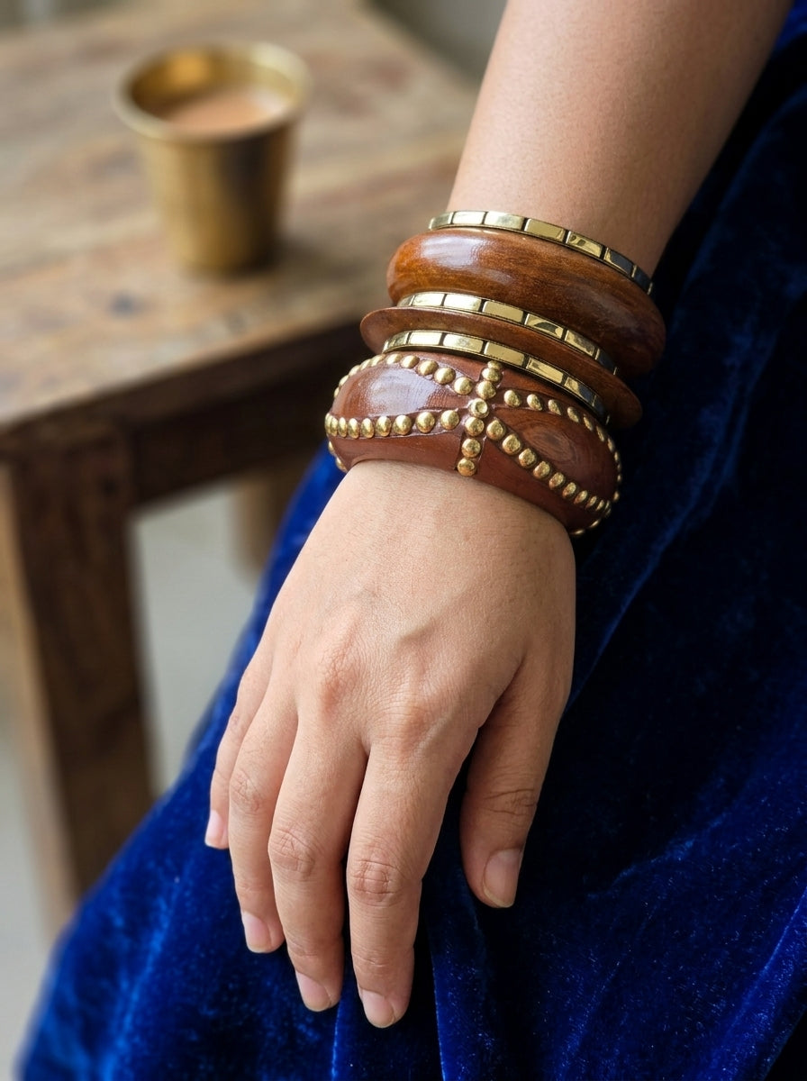 Wooden bangle set styled on a woman's wrist over a rich blue velvet outfit with brass cup in background
